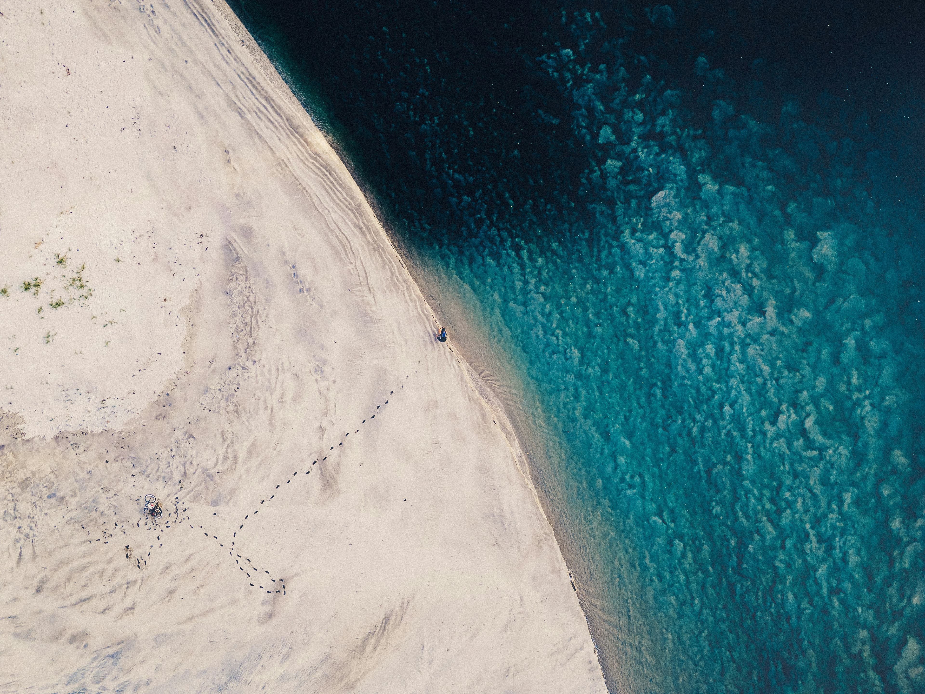 Aerial view of a curved white sand beach meeting turquoise ocean, with a lone figure walking in the sand.
