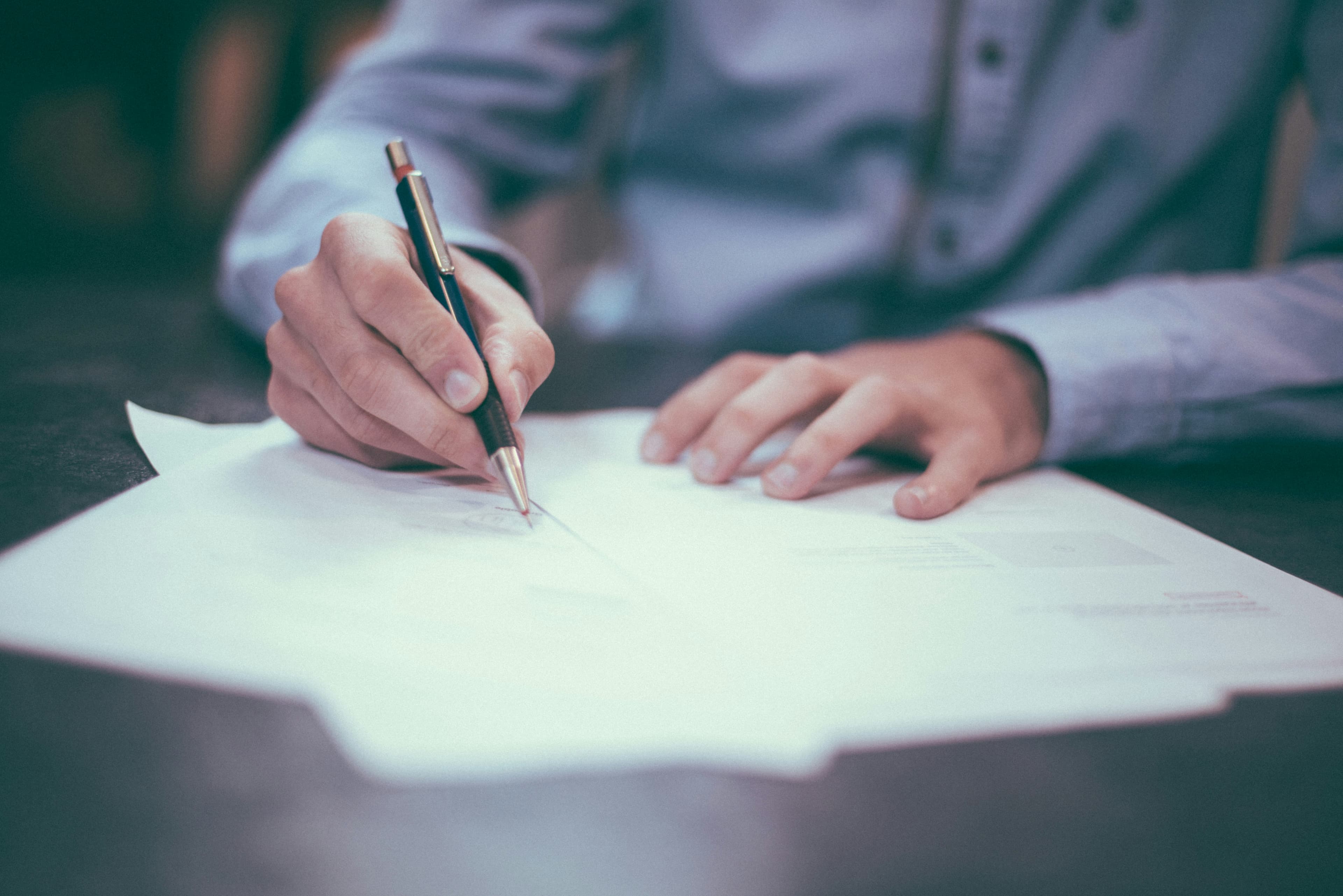 A person's hands signing a document with a pen at a desk.