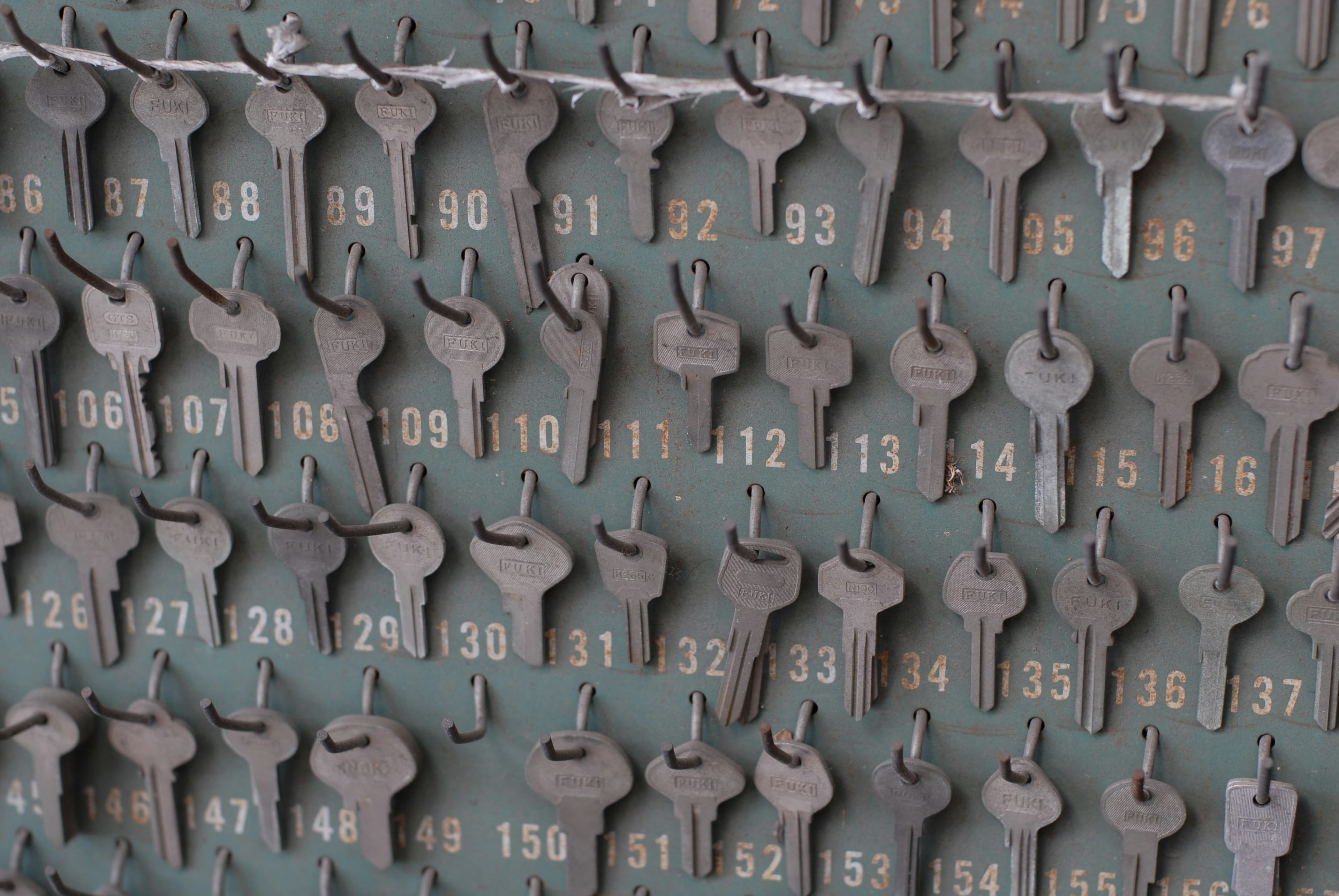 A wall of numbered key hooks on a worn green board, each holding a metal key stamped with the maker's name.