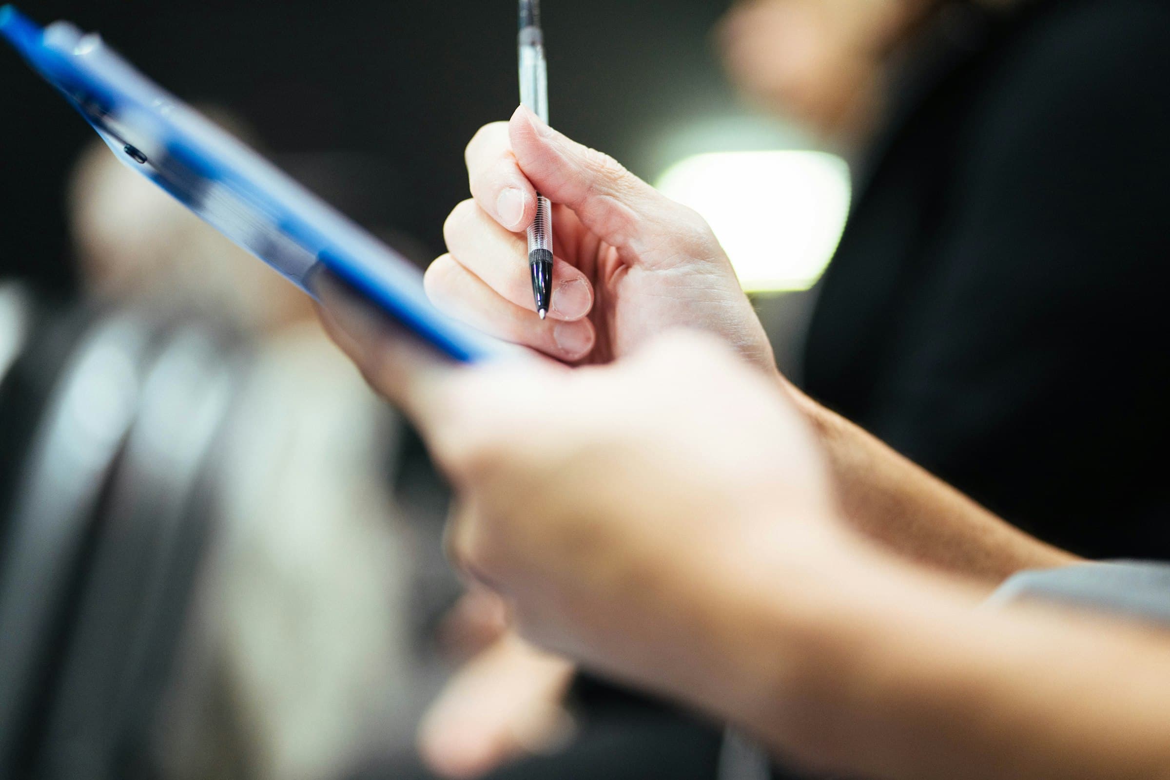A hand holding a pen over a blue clipboard.