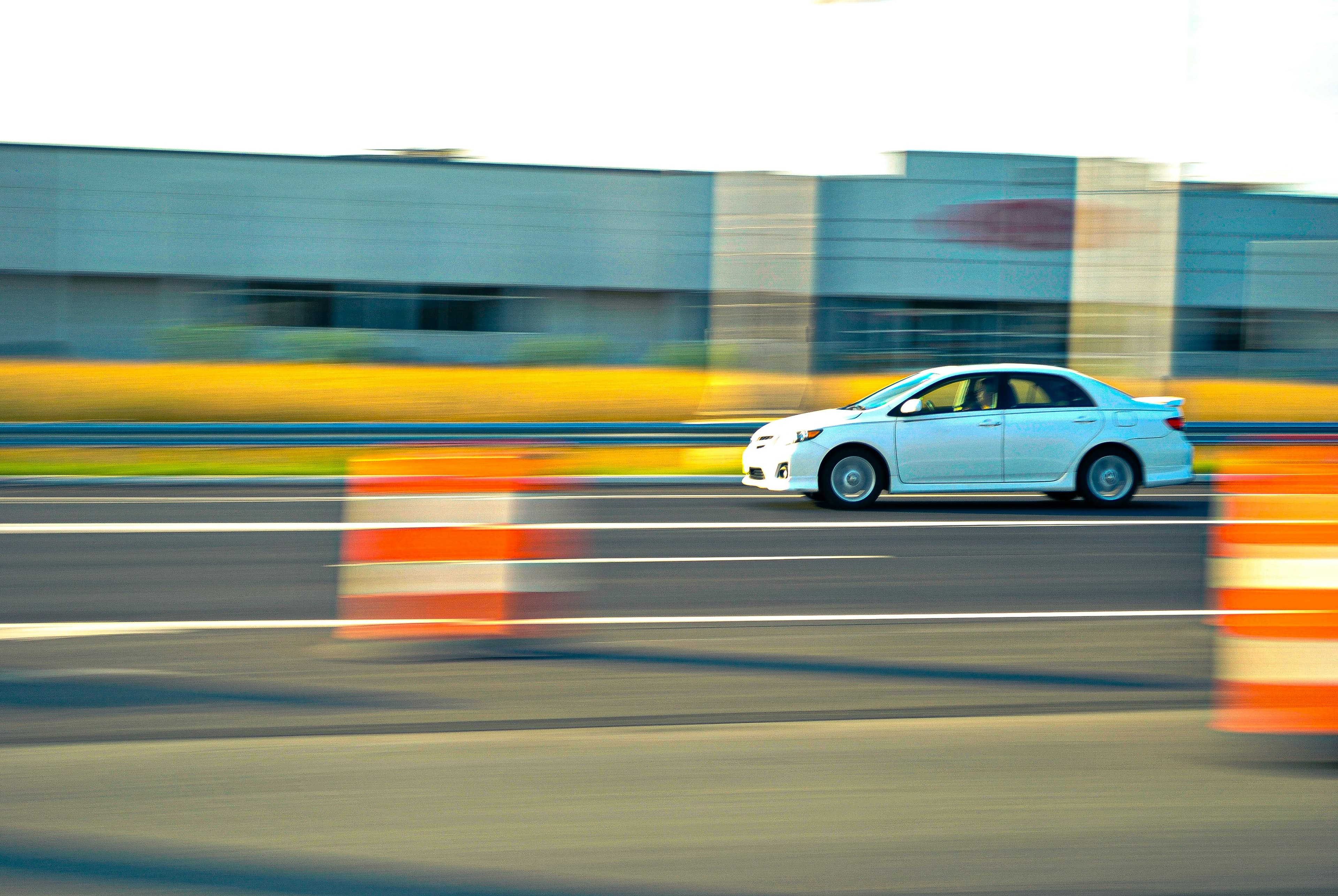 A white sedan in motion on a road, the background blurred by the pan.