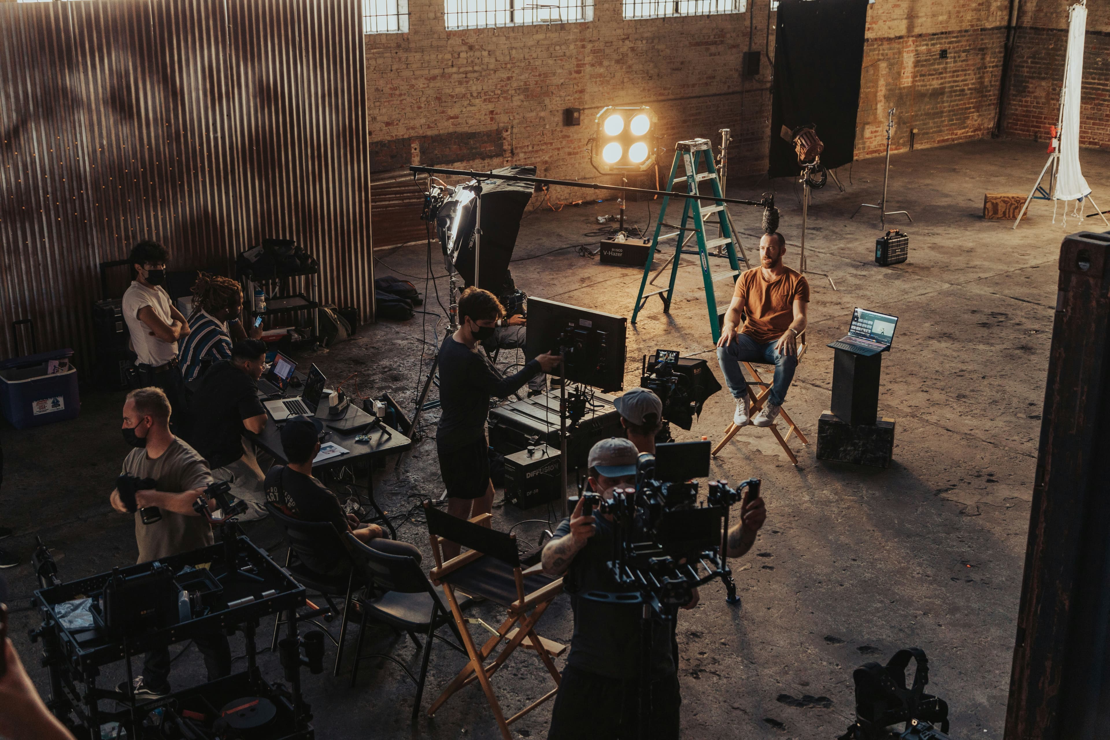 A behind-the-scenes film production set: lighting rigs, monitors, and crew in an industrial warehouse, the shot dressed and everything off-frame whatever was handy.
