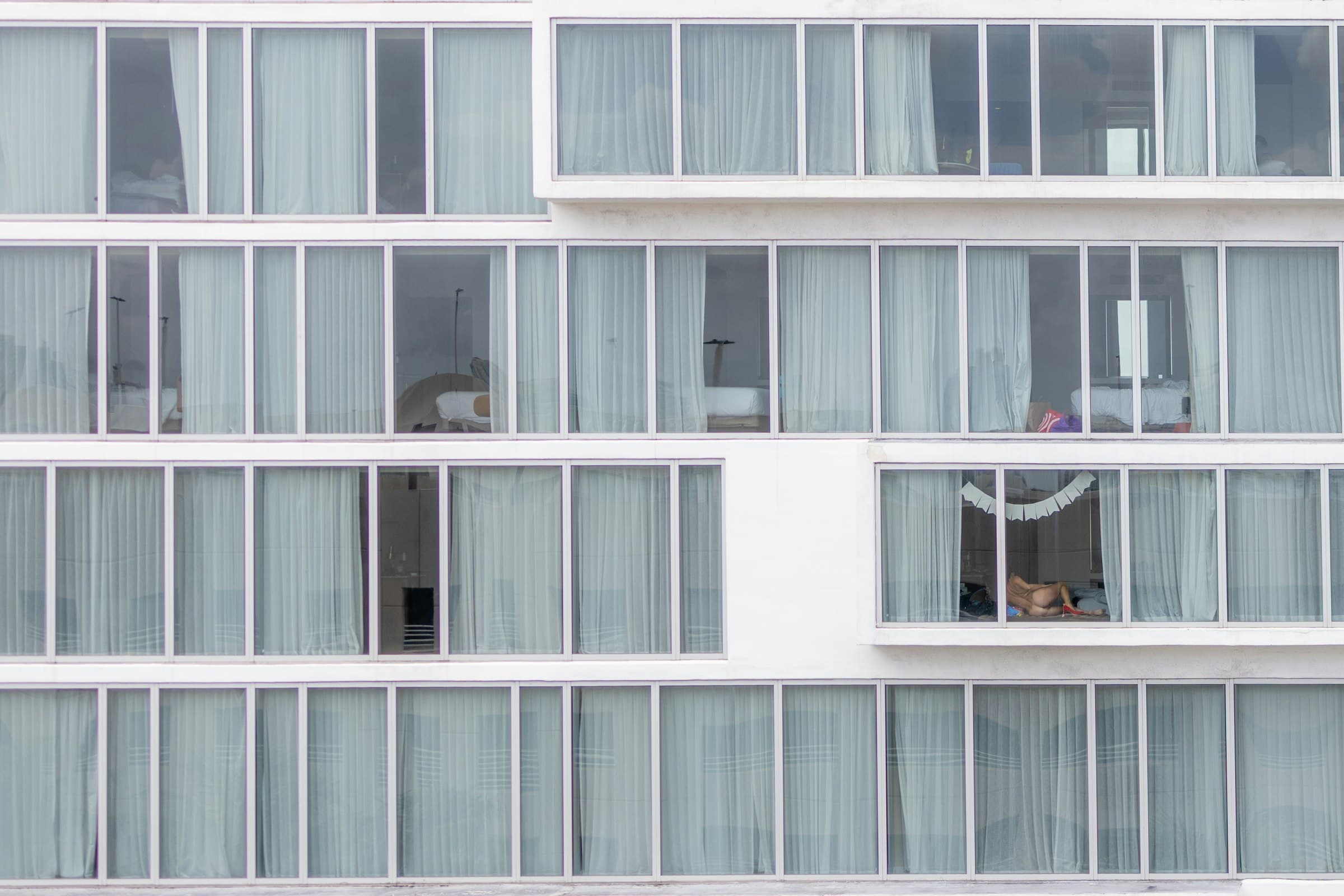 A modern hotel facade with rows of glass windows and white curtains.
